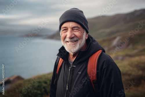 Portrait of happy senior man with backpack standing on top of mountain and looking at camera