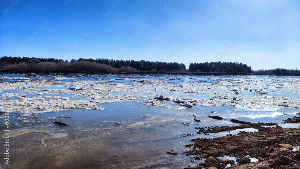 Spring landscape with water and ice on river and blue sky in the background in sunny day. Ice drift and flood on river with sun