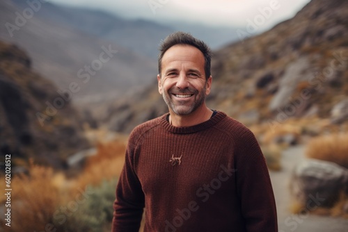 Handsome man in a brown sweater smiling at the camera in the mountains