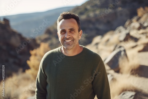 Medium shot portrait photography of a grinning man in his 40s wearing a cozy sweater against a mountain valley or canyon background. Generative AI