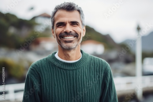 Portrait of handsome mature man in green sweater smiling at camera outdoors