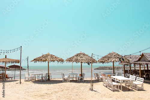Wooden seaside parasols  Straw Umbrellas  and seats with table on the sand beach landscape in clear blue sky for vacation concept in summer holiday