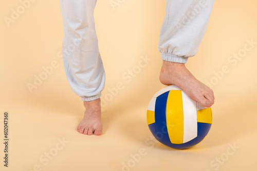 Young volleyball athlete puts one foot on a ball. Girl placed one leg on a ball. Isolated on pastel orange, peach background.