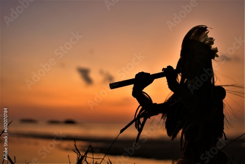 A Native American Indian plays music on a bamboo flute.
 photo