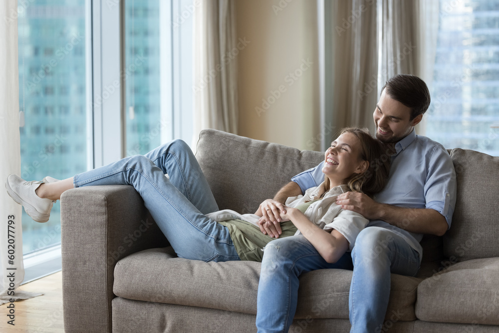 Happy young husband and wife resting on cozy sofa together, laughing, having fun, talking, chatting, enjoying dating, romantic leisure at home, good warm relationships, flirt Happy young husband and wife resting on cozy sofa together, laughing, having fun, talking, chatting, enjoying dating, romantic leisure at home, good warm relationships, flirt