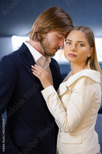 Loving man in a trendy suit gently holds his girlfriend's hand looks into her eyes at a high-end jewelry boutique. Woman has beautifully cared for skin face wears an exquisite diamond gold ring.