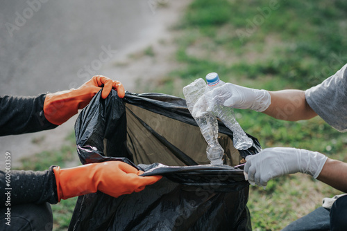 Male hand picking up plastic waste to clean up at the park.