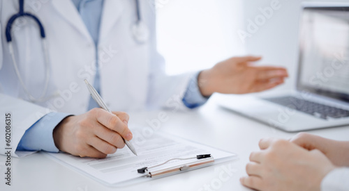 Doctor and patient discussing current health questions while sitting near of each other and using clipboard at the table in clinic, just hands closeup. Medicine concept