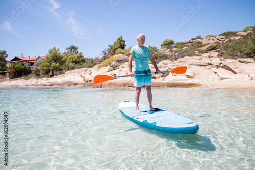Middle aged man having fun, standing with a paddle on a board in the water. SUP. Standup paddleboarding in summer