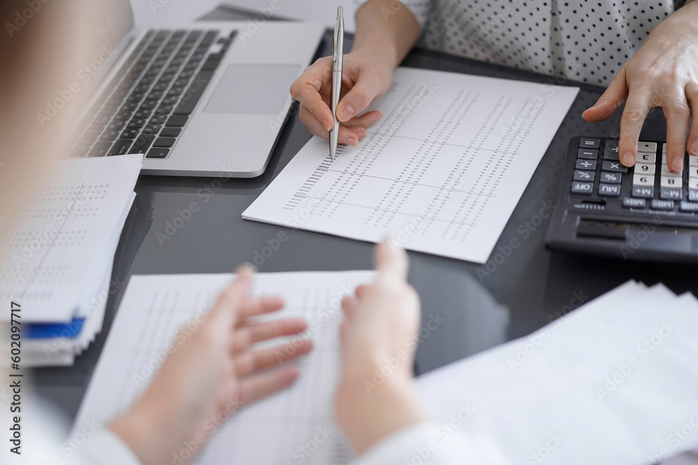 Woman accountant using a calculator and laptop computer while counting taxes with a client or colleague. Business audit team Woman accountant using a calculator and laptop computer while counting taxes with a client or colleague. Business audit team