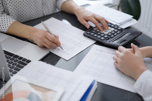 Woman accountant using a calculator and laptop computer while counting taxes with a client or colleague. Business audit team