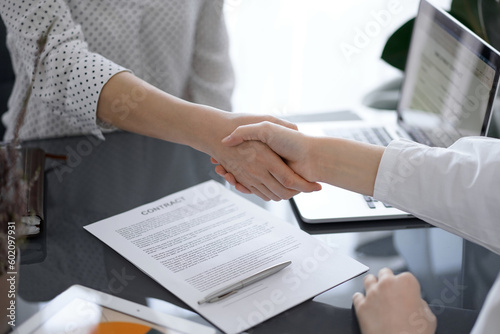 Business people shaking hands above contract papers just signed on the white table, closeup. Lawyers at meeting. Teamwork, partnership, success concept