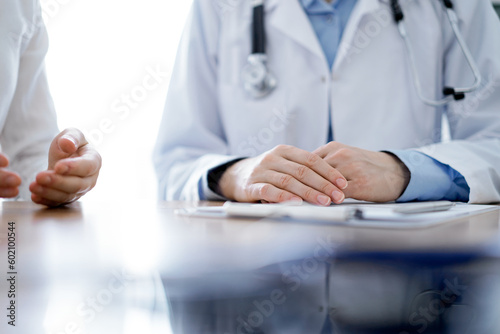 Doctor and patient discussing something while sitting near each other at the wooden desk in clinic, view from above. Medicine concept