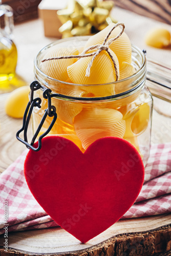 Lumaconi pasta in a glass jar on a wooden background. Red heart and gift. Valentine s Day. selective focus