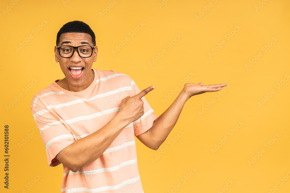 Portrait of happy young african american man in casual smiling, pointing aside with finger, isolated over yellow background.