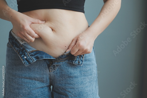 Close up of a belly with scar from c-section and abdominal fat. Women's health. A woman dressed up in sportswear demonstrating her imperfect body after a childbirth with nursery on the background. © ARMMY PICCA