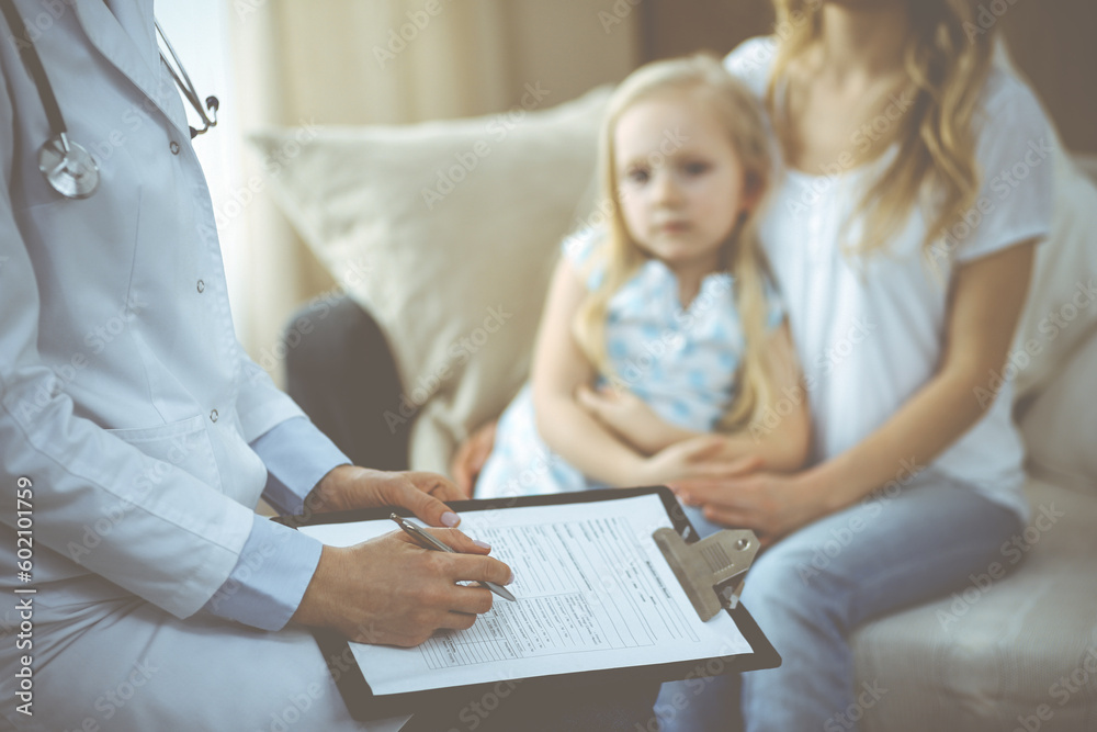 Doctor and patient. Pediatrician using clipboard while examining little girl with her mother at home. Happy cute caucasian child at medical exam. Medicine concept Doctor and patient. Pediatrician using clipboard while examining little girl with her mother at home. Happy cute caucasian child at medical exam. Medicine concept