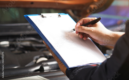 Services car engine machine concept, Automobile mechanic repairman checking a car engine with inspecting writing to the clipboard the checklist for repair machine, car service and maintenance.