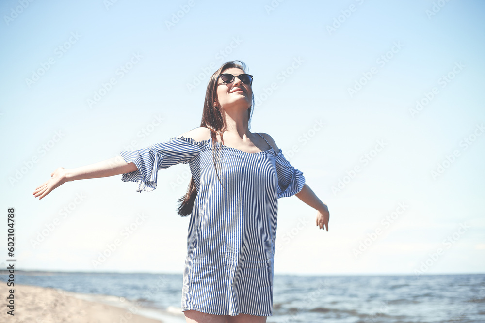 Happy young brunette woman relaxing on a wooden deck chair at the ocean beach while smiling, and wearing fashion sunglasses. The enjoying vacation concept Happy young brunette woman relaxing on a wooden deck chair at the ocean beach while smiling, and wearing fashion sunglasses. The enjoying vacation concept