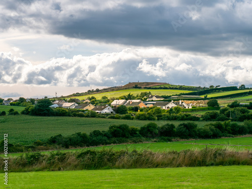 Sky with cumulus clouds over a Irish village on a summer evening. Irish settlement in County Cork, dramatic landscape. European countryside, rustic landscape. Green grass field under cloudy sky