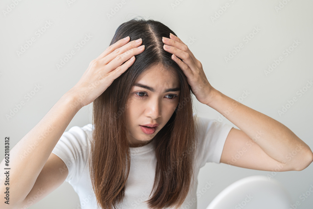 Damaged Hair symptom, face serious asian young woman, girl worry about balding, looking at scalp in mirror, hand in break into front hair loss, thin problem. Health care treatment for beauty concept.