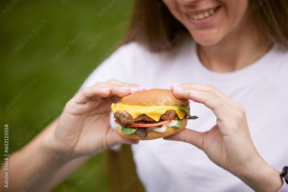 a young girl takes out a burger from a paper bag sitting on the green grass, the concept of food delivery, street food a young girl takes out a burger from a paper bag sitting on the green grass, the concept of food delivery, street food