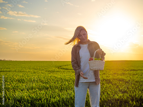 A female farmer with a basket of fresh vegetables and fruit walks along the field. Health concept