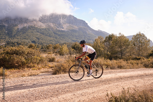 Cyclist practicing on gravel road.Fit male cyclist riding a gravel bike on a gravel road with a view of the mountains, Alicante region of Spain photo