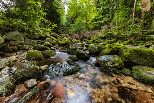 Beautiful small waterfall full of small and big rocks and stones with green trees around next to mountain trail in Giant mountains