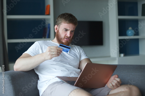Nervous sad upset confused young man, stressed worried guy having problem with paying, buying online, payments with credit blocked bank card, looking at screen, monitor of laptop. Internet fraud