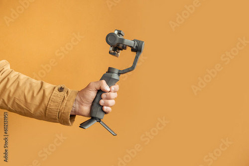 Man hand filming with a smartphone using a gimbal stabilizer on yellow background. Using three-axis electronic stabilizer to make vlogs or video shooting. Copy space for a free text