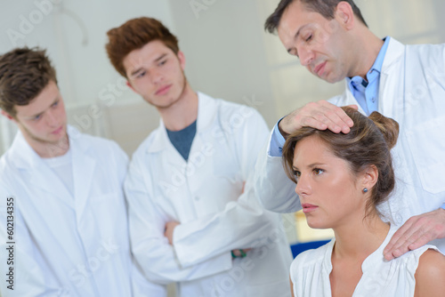 Students observing doctor with hand on patient's head and shoulder
