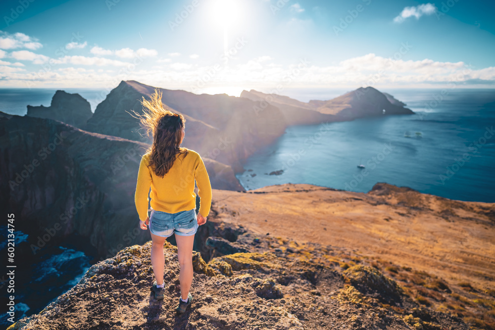 Fototapeta premium Back view of a woman looking at the foothills of a volcanic island in the Atlantic Ocean from a panoramic morning viewpoint. São Lourenço, Madeira Island, Portugal, Europe.