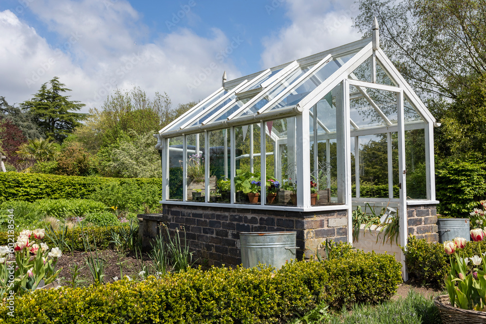 A garden plot with seedbeds and a glass greenhouse in the center of kitchen garden. A suburban or rustic backyard for gardening. A warm summers day.Trentham gardens staffordshire A garden plot with seedbeds and a glass greenhouse in the center of kitchen garden. A suburban or rustic backyard for gardening. A warm summers day.Trentham gardens staffordshire