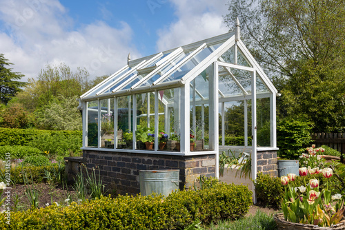 A garden plot with seedbeds and a glass greenhouse in the center of kitchen garden. A suburban or rustic backyard for gardening. A warm summers day.Trentham gardens staffordshire