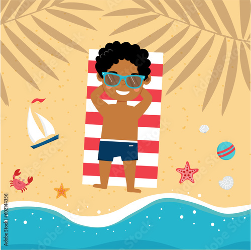 Little african american boy is lying on the beach and sunbathing on towel in the shade of palm trees on the beach. Cute little boy on vacation. Summer time, holiday.