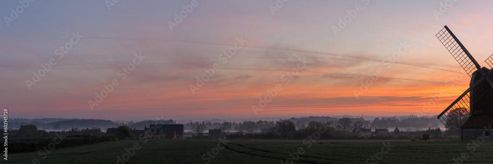 Panorama view of View of English countryside on a misty morning at dawn with partial view of windmill
