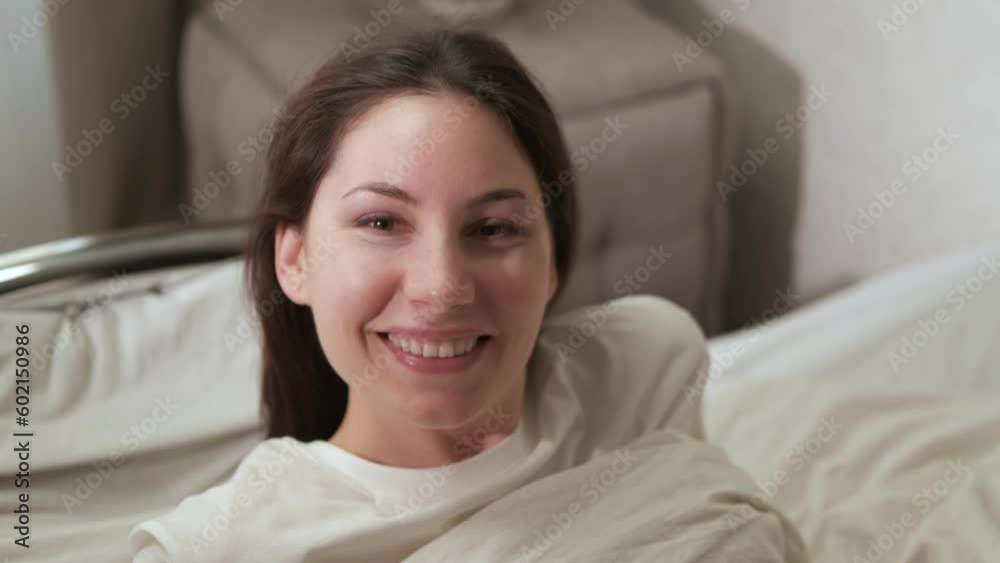 An attractive young woman is sitting on a bed in the early sunny morning, smiling and looking at the camera. Close up An attractive young woman is sitting on a bed in the early sunny morning, smiling and looking at the camera. Close up
