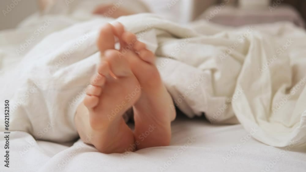 Women's feet itch in bed under a white blanket. Foot diseases, fungus