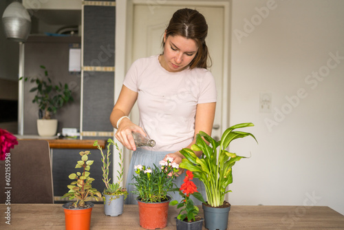 Young woman taking care of her potted plants at her living room.