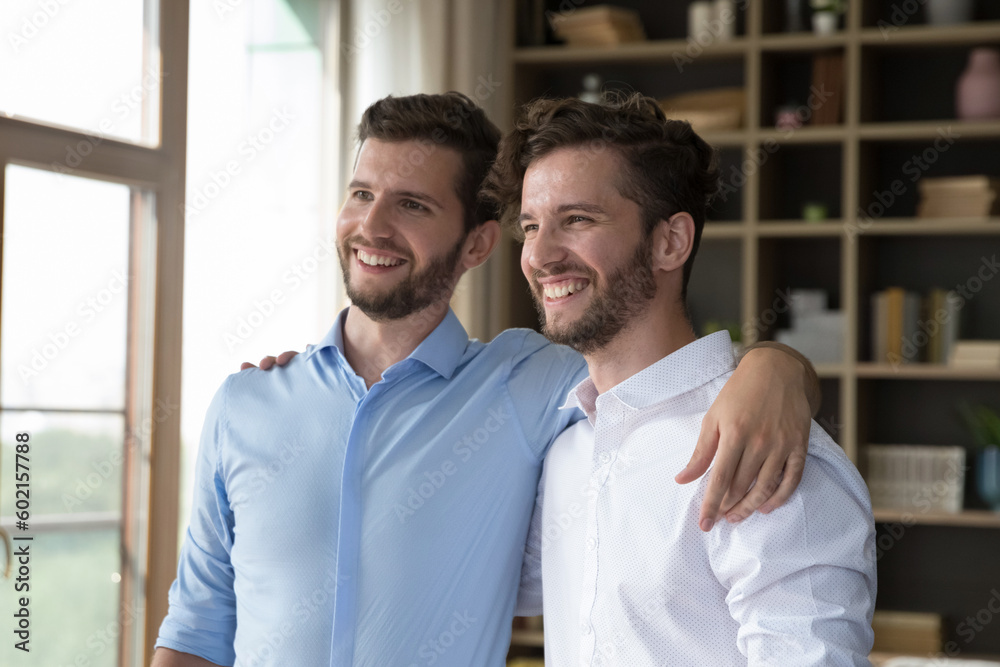 Cheerful handsome young adult twin brothers posing for shooting together, standing close, hugging, patting shoulders, looking away, smiling, laughing, enjoying friendship Cheerful handsome young adult twin brothers posing for shooting together, standing close, hugging, patting shoulders, looking away, smiling, laughing, enjoying friendship