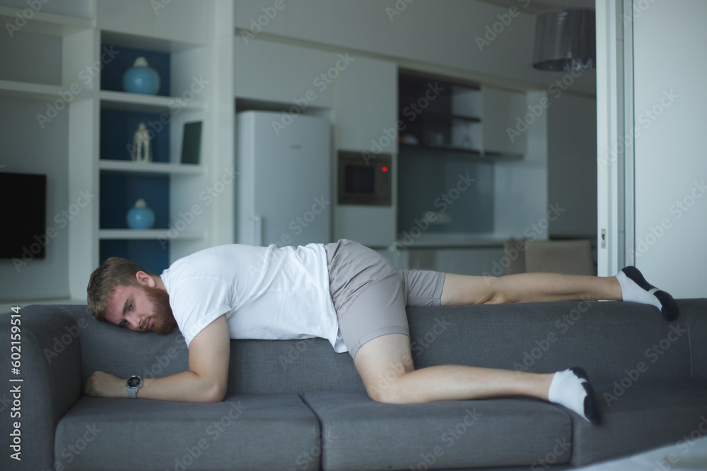 Exhausted young man fell asleep on comfortable couch in modern living room, having no energy after hard working day. Tired depressed unmotivated european guy napping on sofa at home, fatigue concept.