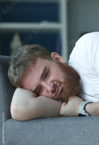 Depressed disappointed man with broken heart because of break up crying abundantly laying on sofa having psychotic moment. Male trying to stifle pain and frustration, psychological suicidal thoughts