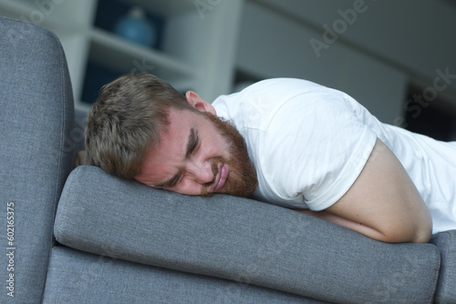 Depressed disappointed man with broken heart because of break up crying abundantly laying on sofa having psychotic moment. Male trying to stifle pain and frustration, psychological suicidal thoughts