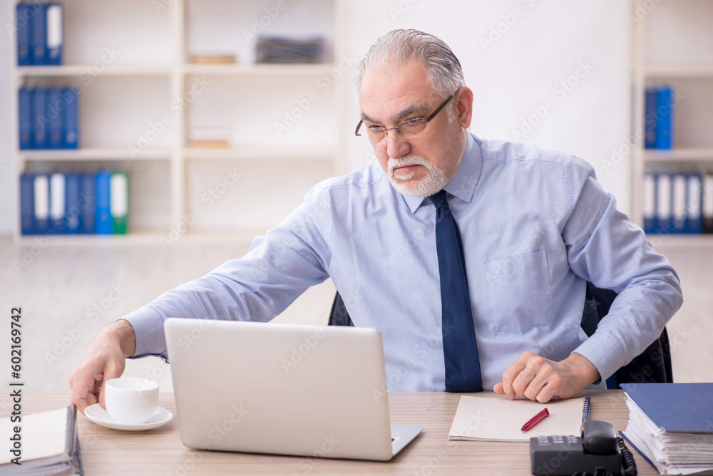 Old male employee drinking tea in the office
