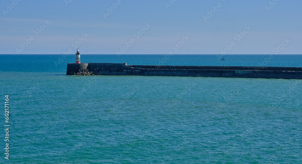 The entrance to Newhaven harbour, East Sussex, UK and its breakwater and lighthouse. Clear blue sky and water  in the background.
