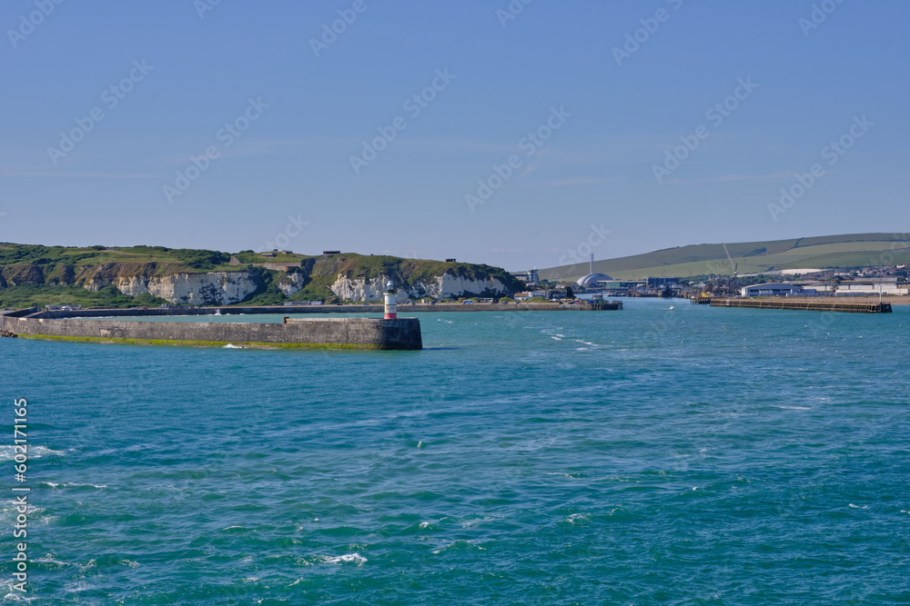 The entrance to Newhaven harbour, East Sussex, UK and its breakwater and lighthouse. Clear blue sky and water with white cliffs in the background.