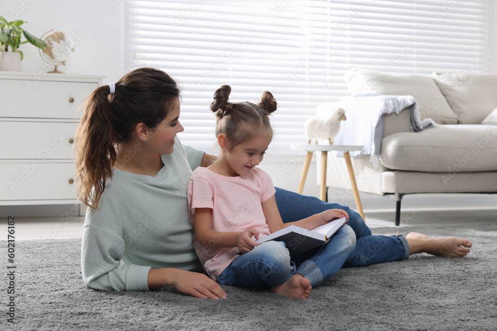 Young mother and her daughter reading book on floor at home