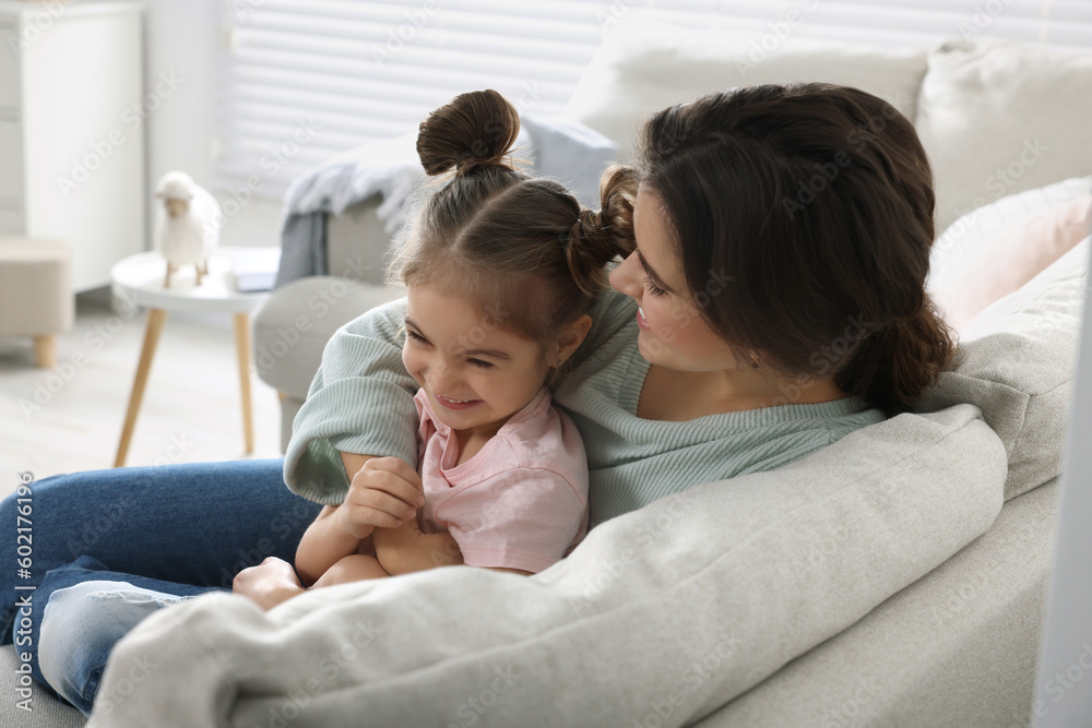 Young mother and her daughter spending time together on sofa at home