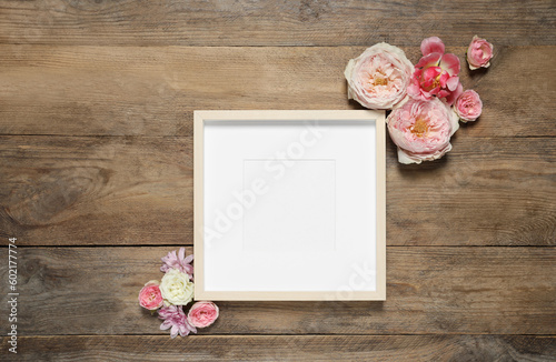 Empty photo frame and beautiful flowers on wooden table, flat lay. Space for design